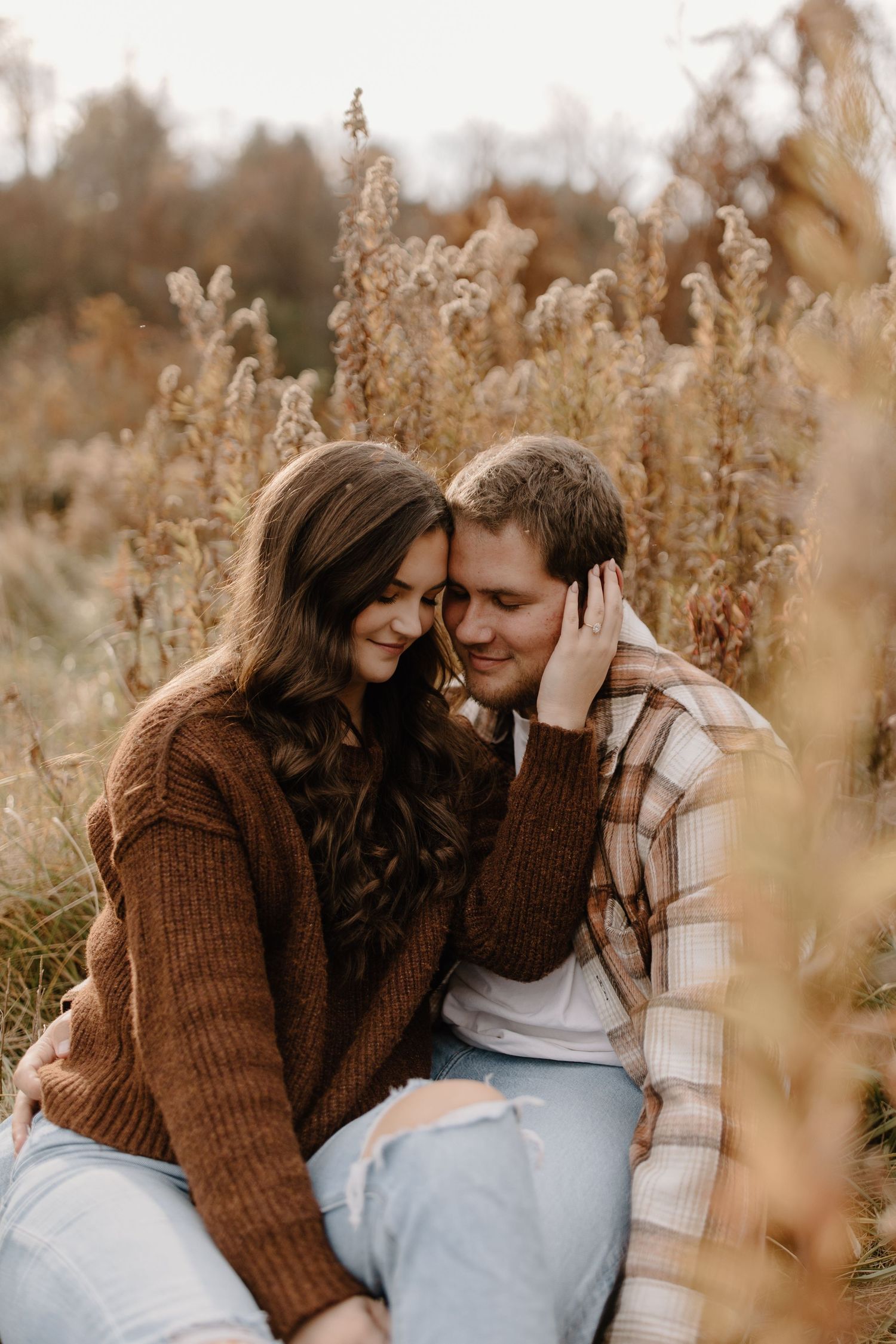 Intimate autumn portrait of a couple embracing among tall dried grasses in warm earth tones.