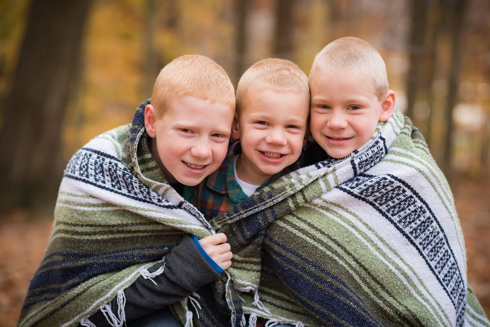 Joyful sibling portrait of three boys wrapped up in a blanket, taken by photographer Laura Priestley in Morgantown, WV