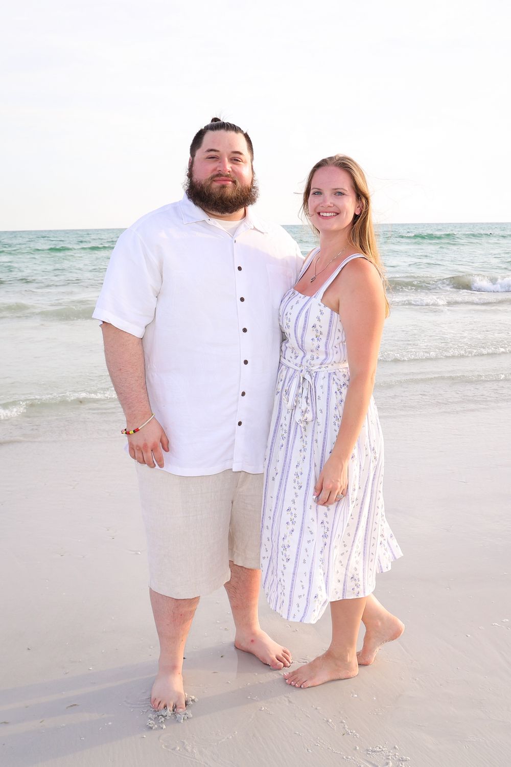 Beach portrait of couple in white outfits standing together on white sand.