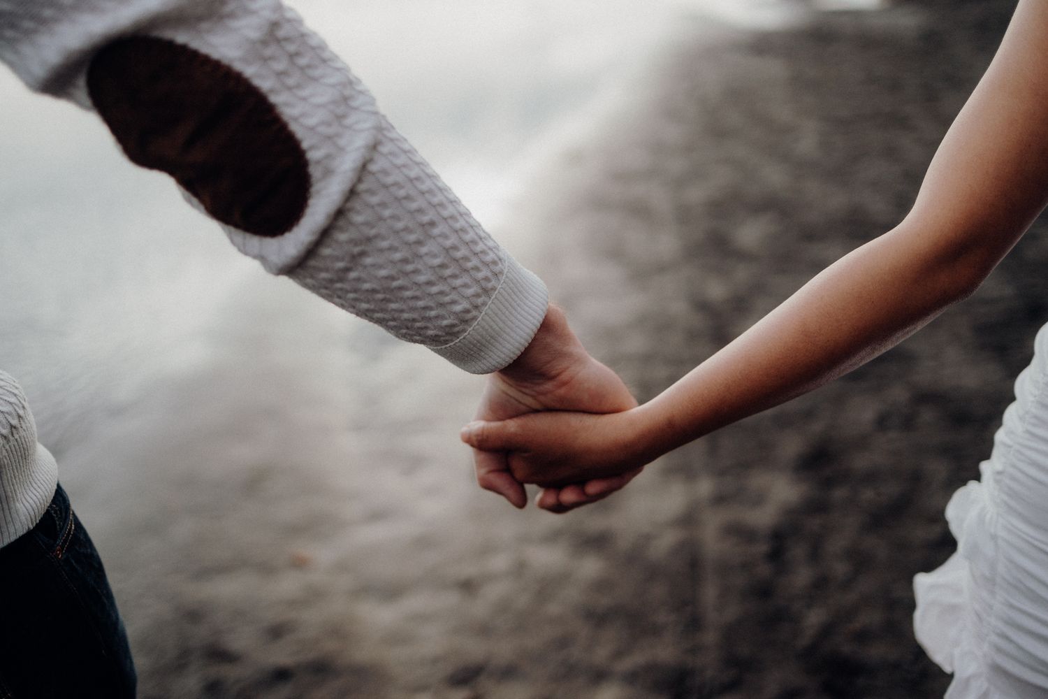 Close-up shot of two people holding hands on a dark sandy beach.