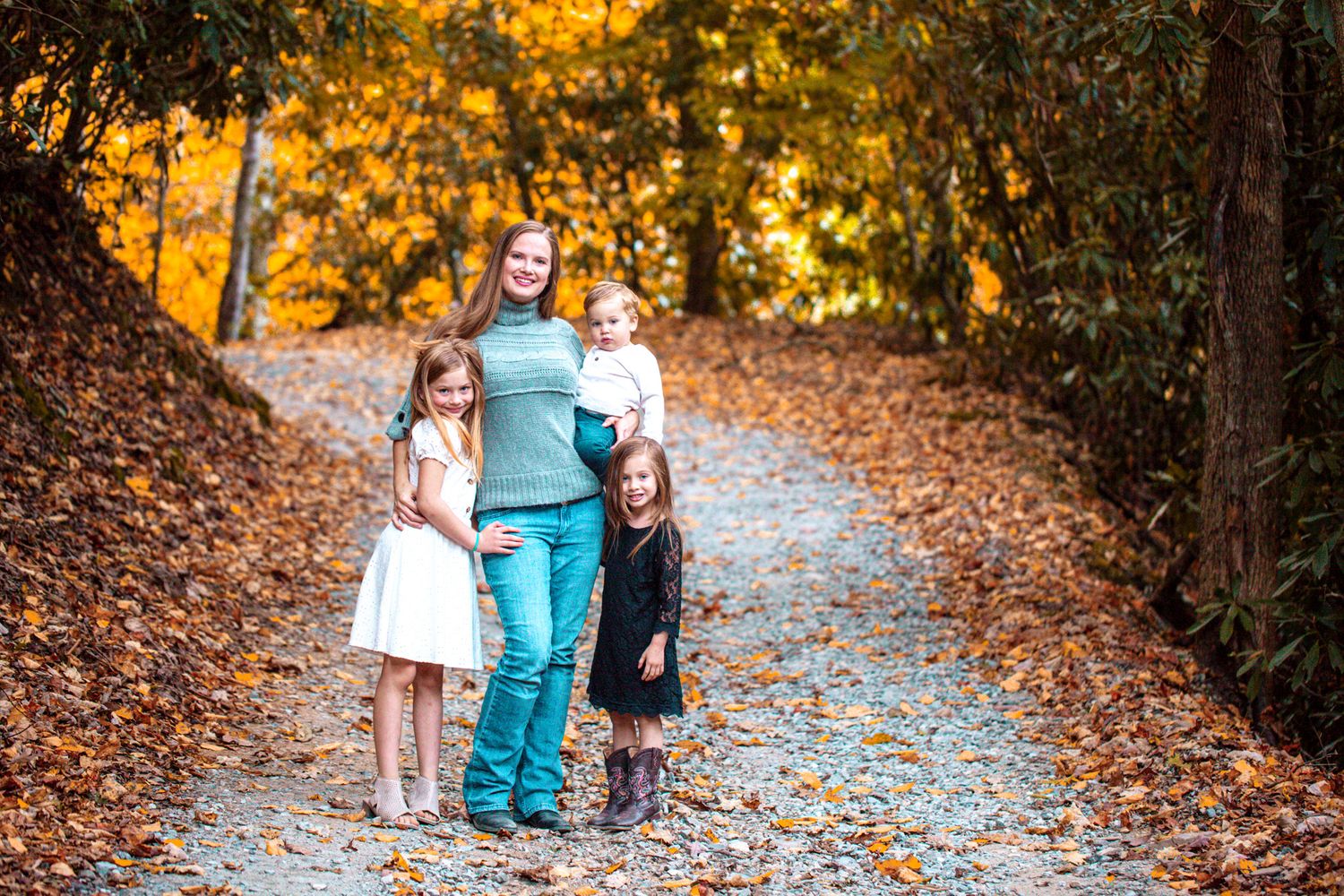 Three people walking together on a leaf-covered autumn trail.