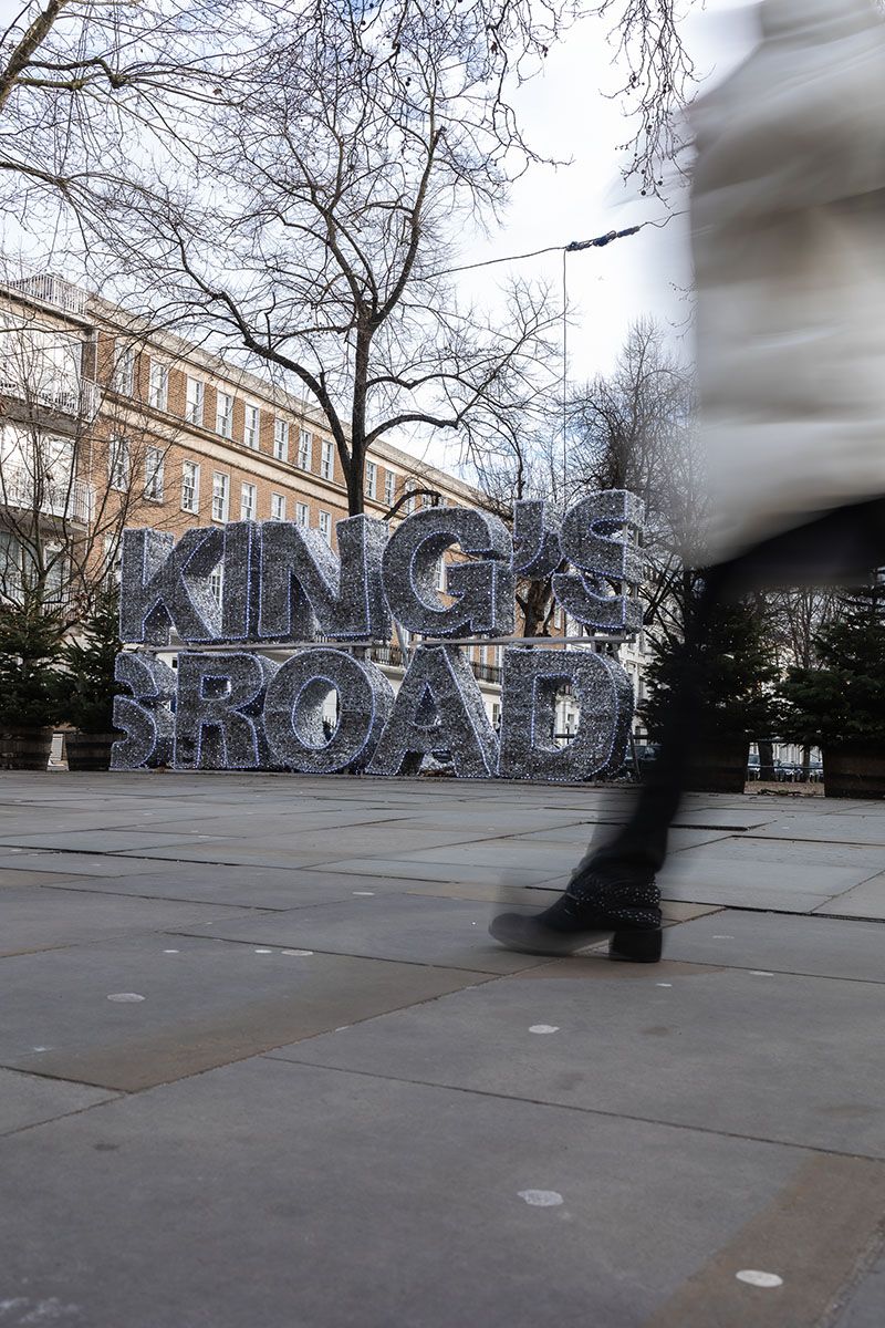 Passerby walking past the Kings Road sign in Chelsea at Christmas time. Christmas lights all around.