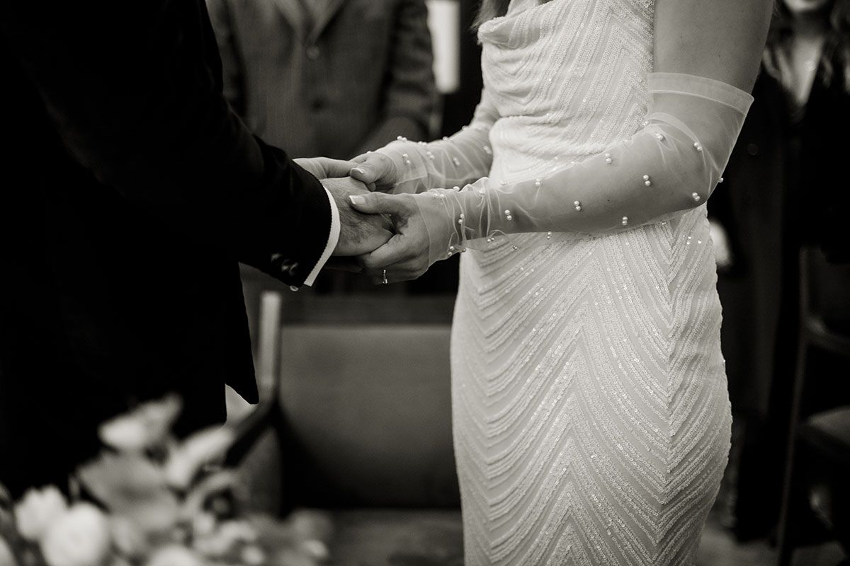 Natural shot of bride and groom holding hands during wedding ceremony in town hall, London