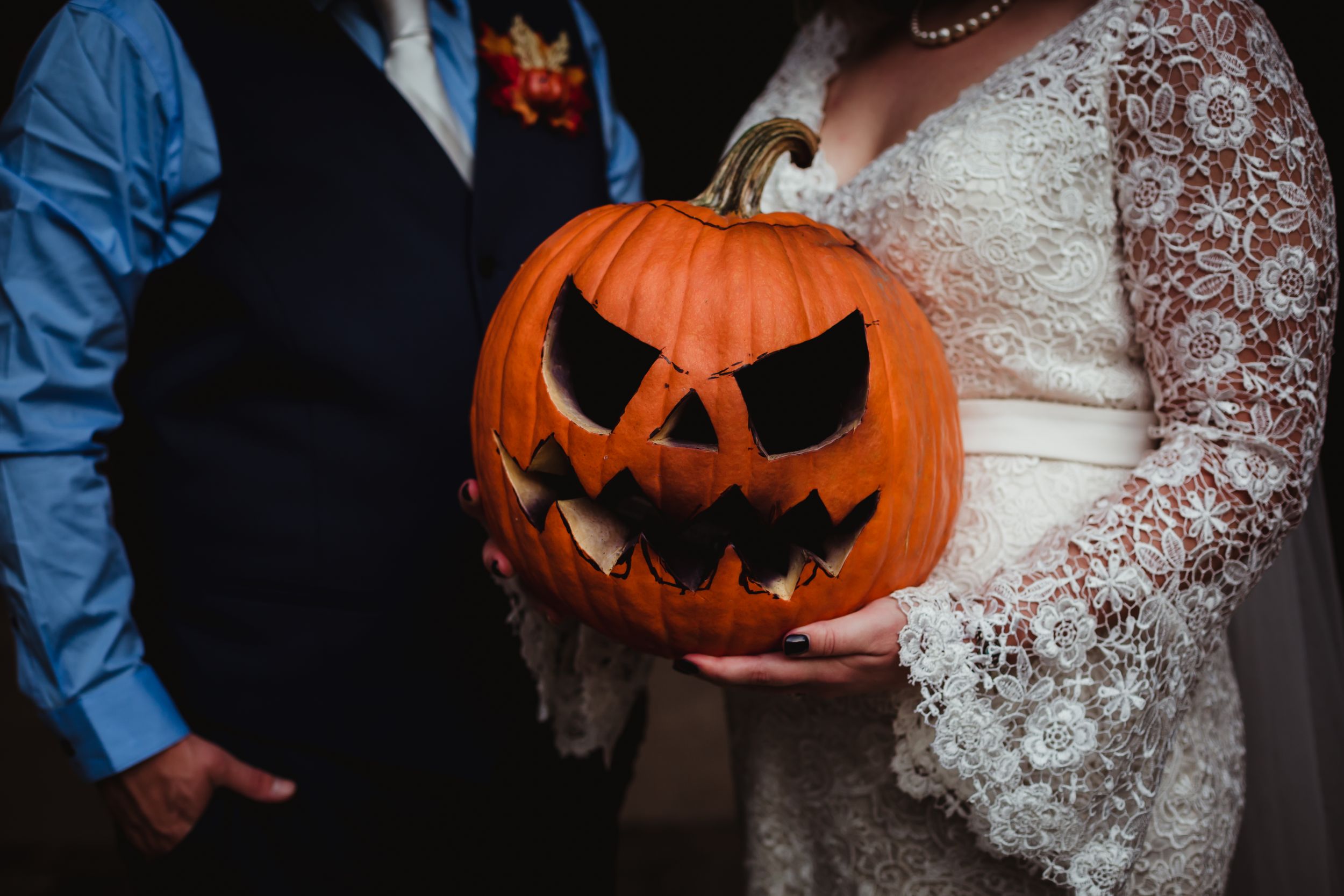 Close up of a jack-o-lantern being held by a man and woman in wedding attire.
