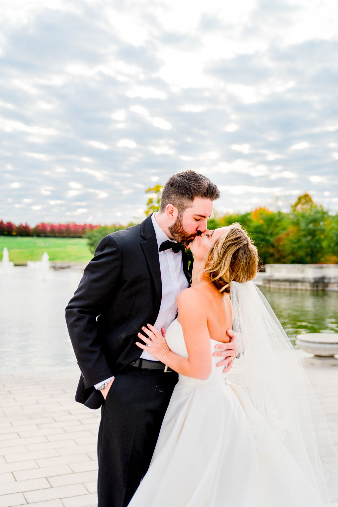 bride's wedding dress and veil fanned out next to groom under blue sky with clouds for Forest Park STL fall wedding