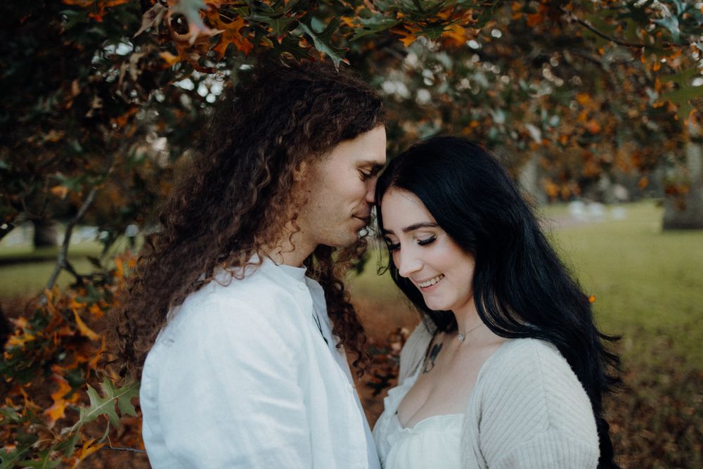 A tender moment between two people beneath autumn trees in a park setting.
