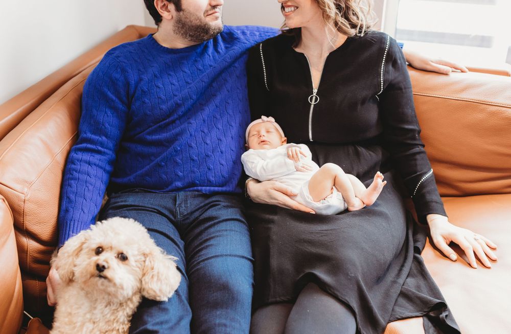 Parents sitting on the sofa with dog holding newborn during their Chicago Lifestyle newborn session