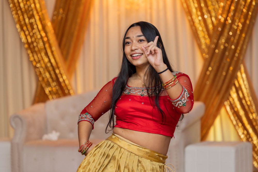 Traditional dancer in red and gold outfit performs with gold sequined backdrop.