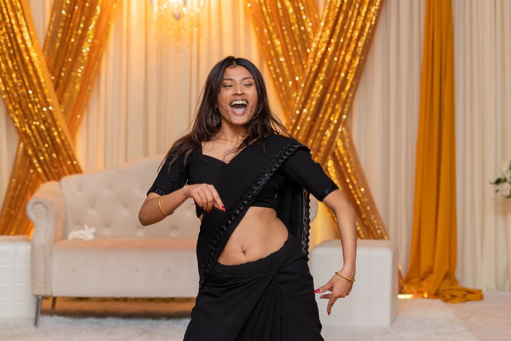 Dancer in black outfit performs with enthusiasm against golden backdrop.