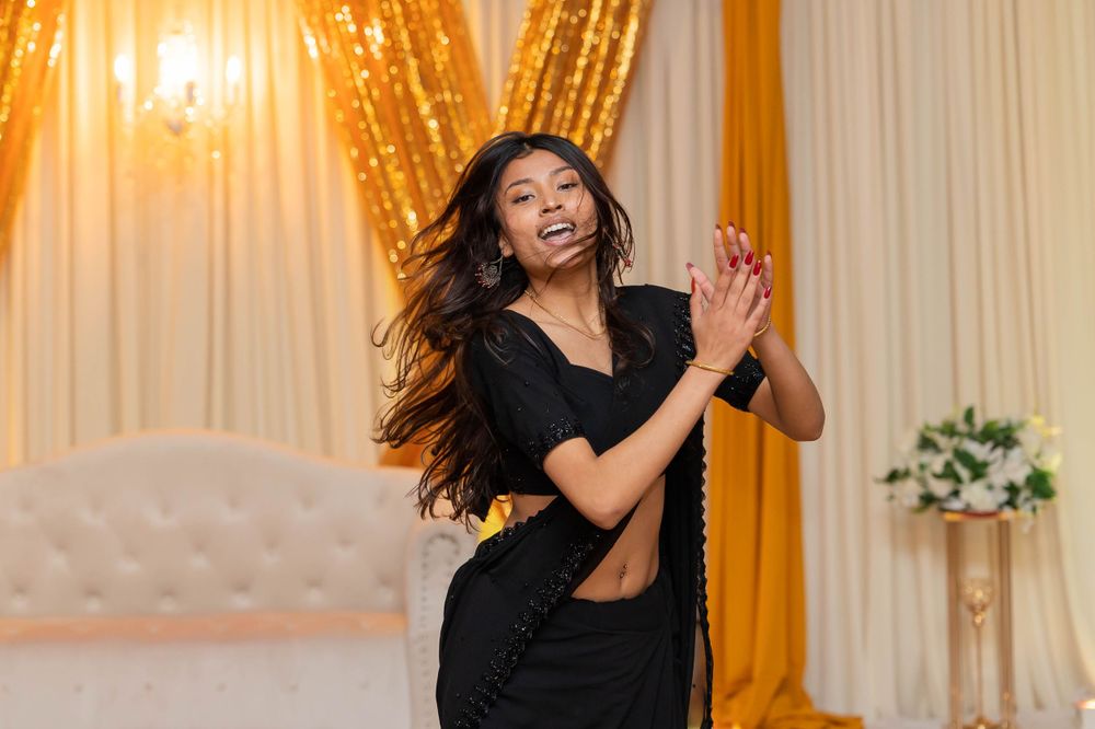 Dancer in black outfit performing energetic moves against golden curtain backdrop.
