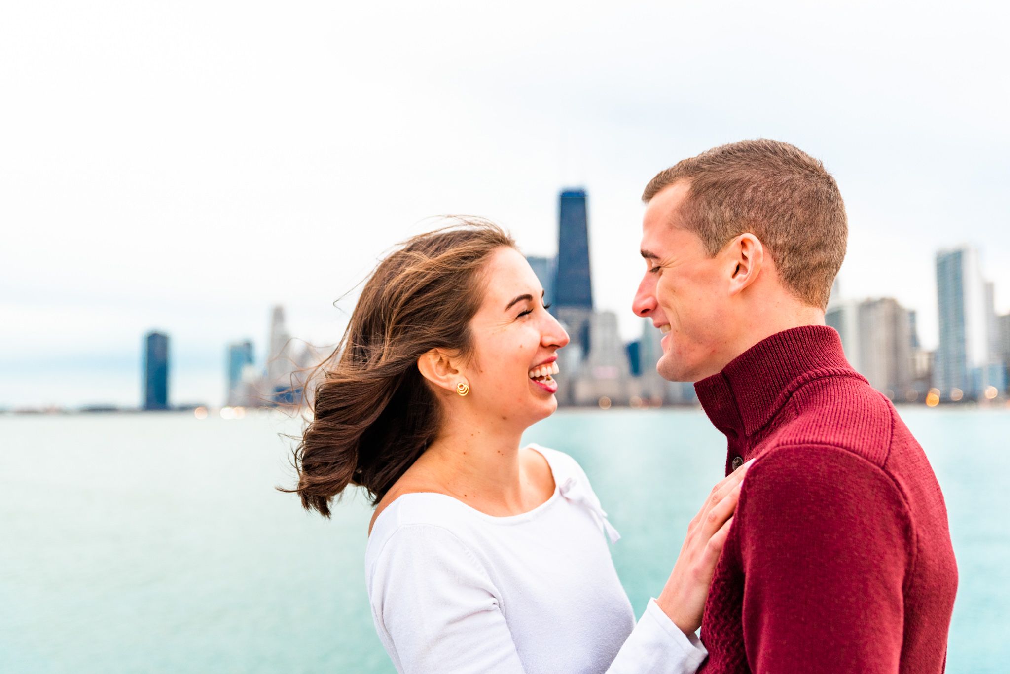 woman with short brown hair smiling at fiance in red sweater at North Avenue Beach engagement pictures
