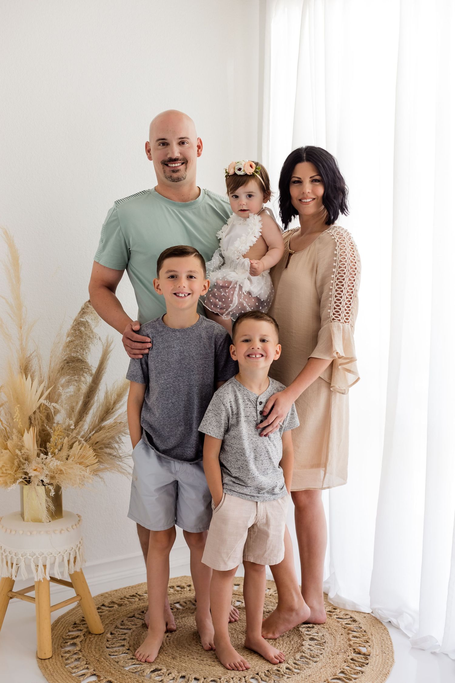 Simple white studio with boho florals and a family of five posing and smiling for the camera during their family portrait session.