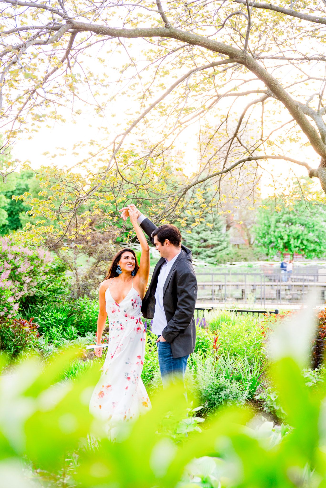 man in gray suit and jeans twirling fiance in Lincoln Park engagement pictures at sunset as she smiles