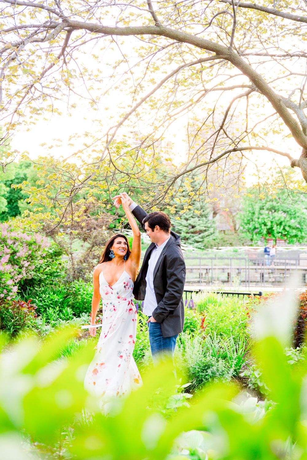 man in gray suit and jeans twirling fiance in Lincoln Park engagement pictures at sunset as she smiles