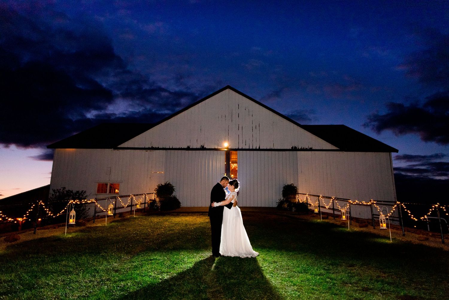newlywed couple standing with faces together under a dark blue sky at night