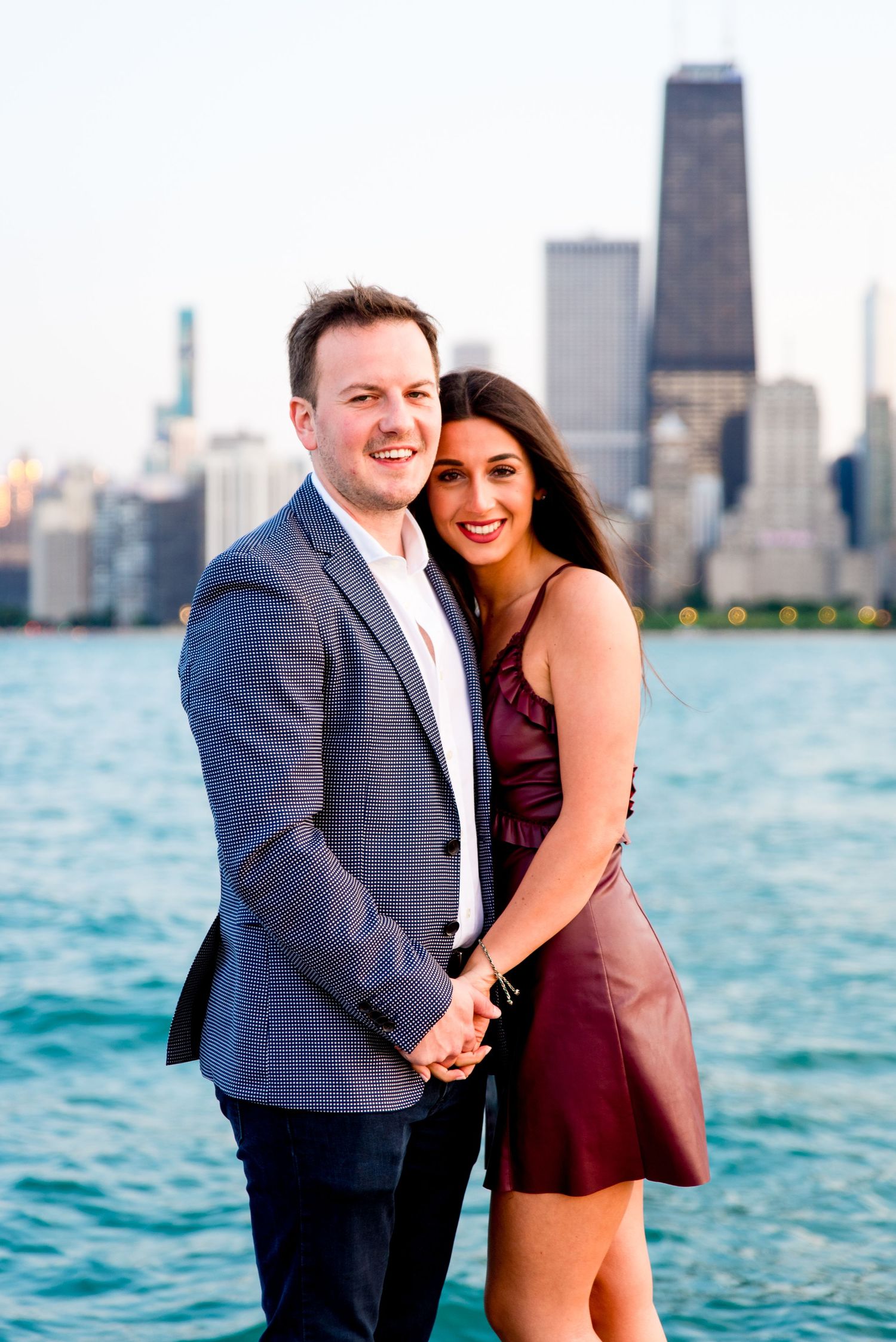 man and woman holding hands looking at camera in front of Chicago skyline + Lake Michigan after North Ave Beach proposal