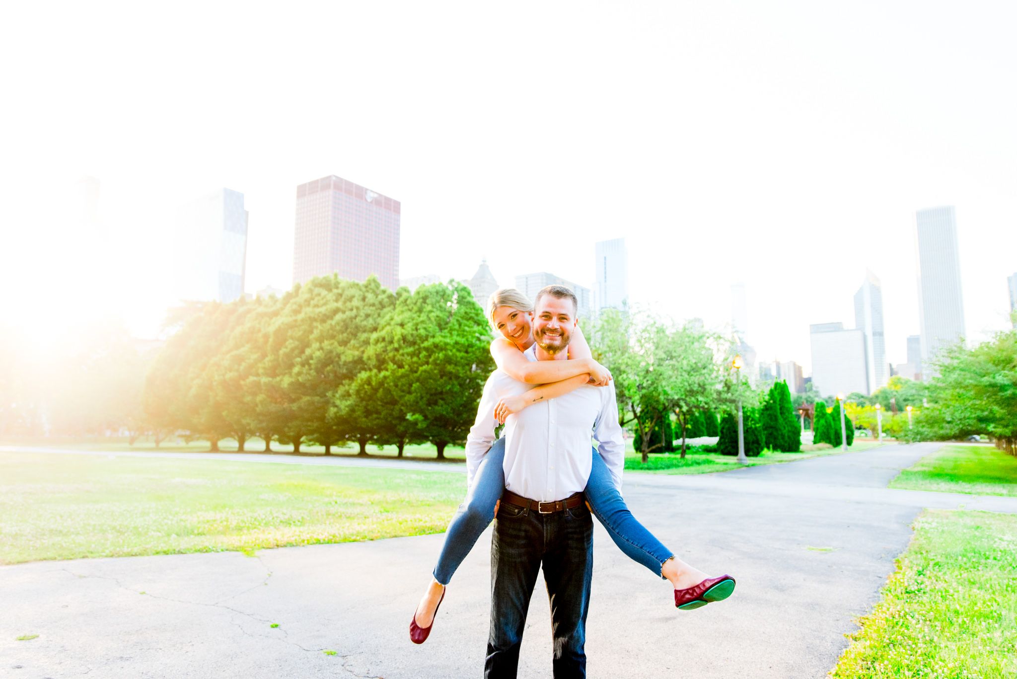 blonde woman in jeans piggy back riding fiance in Grant Park Chicago at sunset