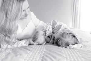 Mother snuggles on a bed with her newborn son and toddler daughter as they lay head first.