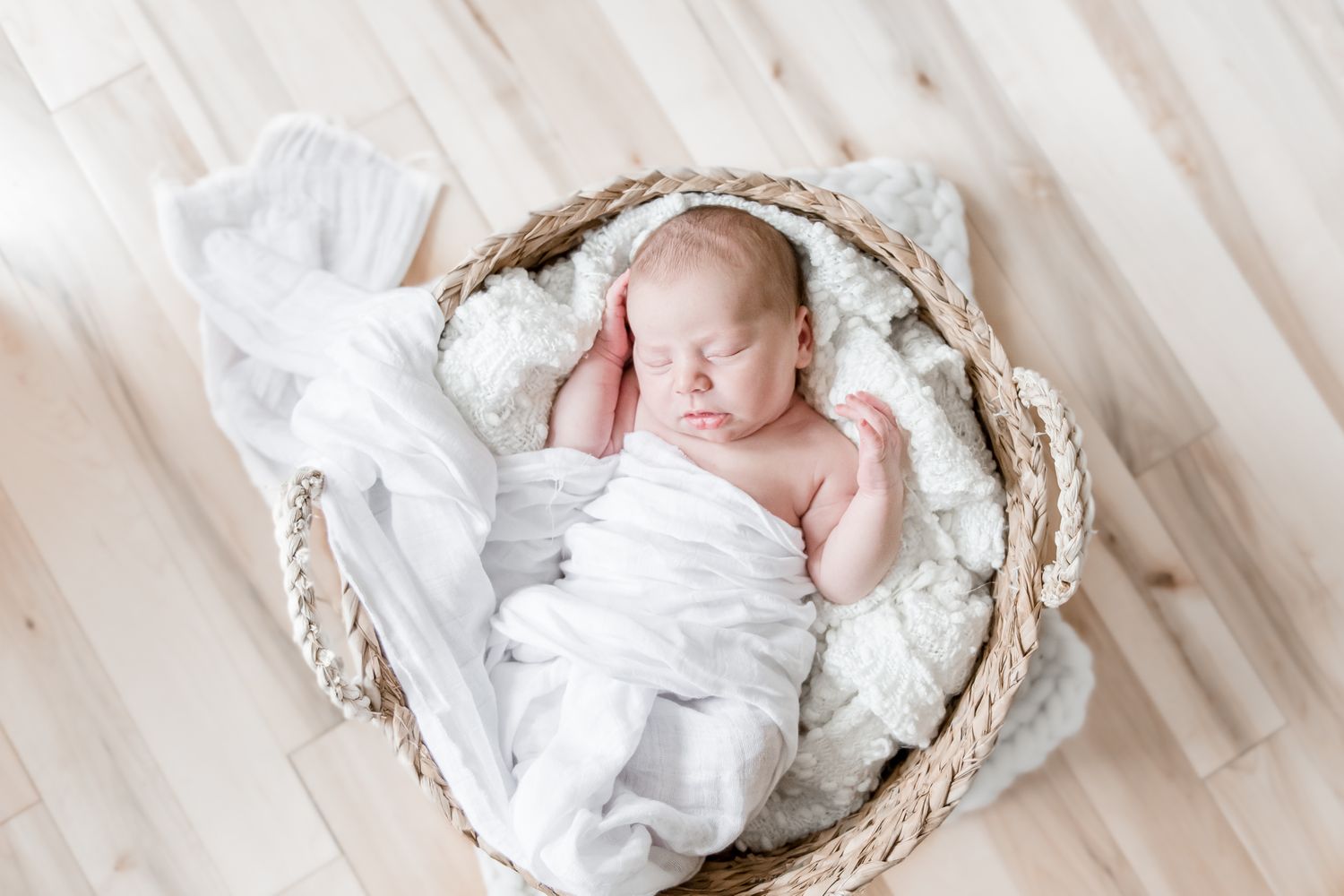 Newborn baby in a wicker basket wrapped in white linens