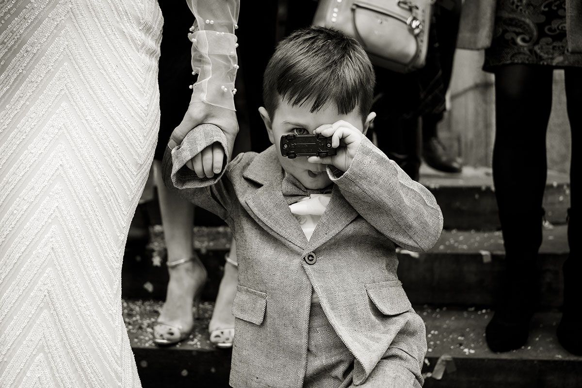 Page boy hiding behind his toy car during group photographs.