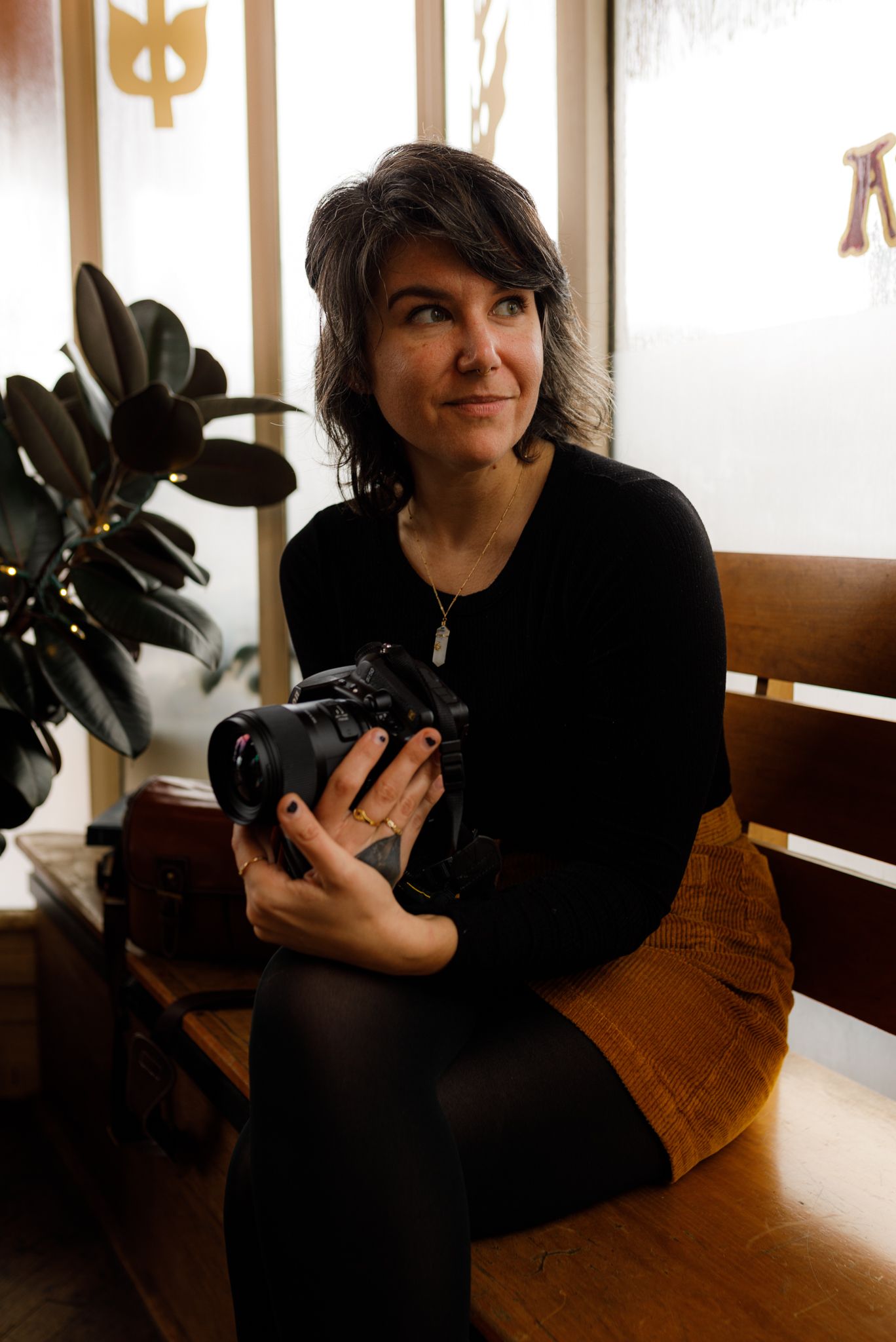 Person holding a camera in a local bakery on a wooden bench in Richmond, Virginia smiling softly with warm natural light