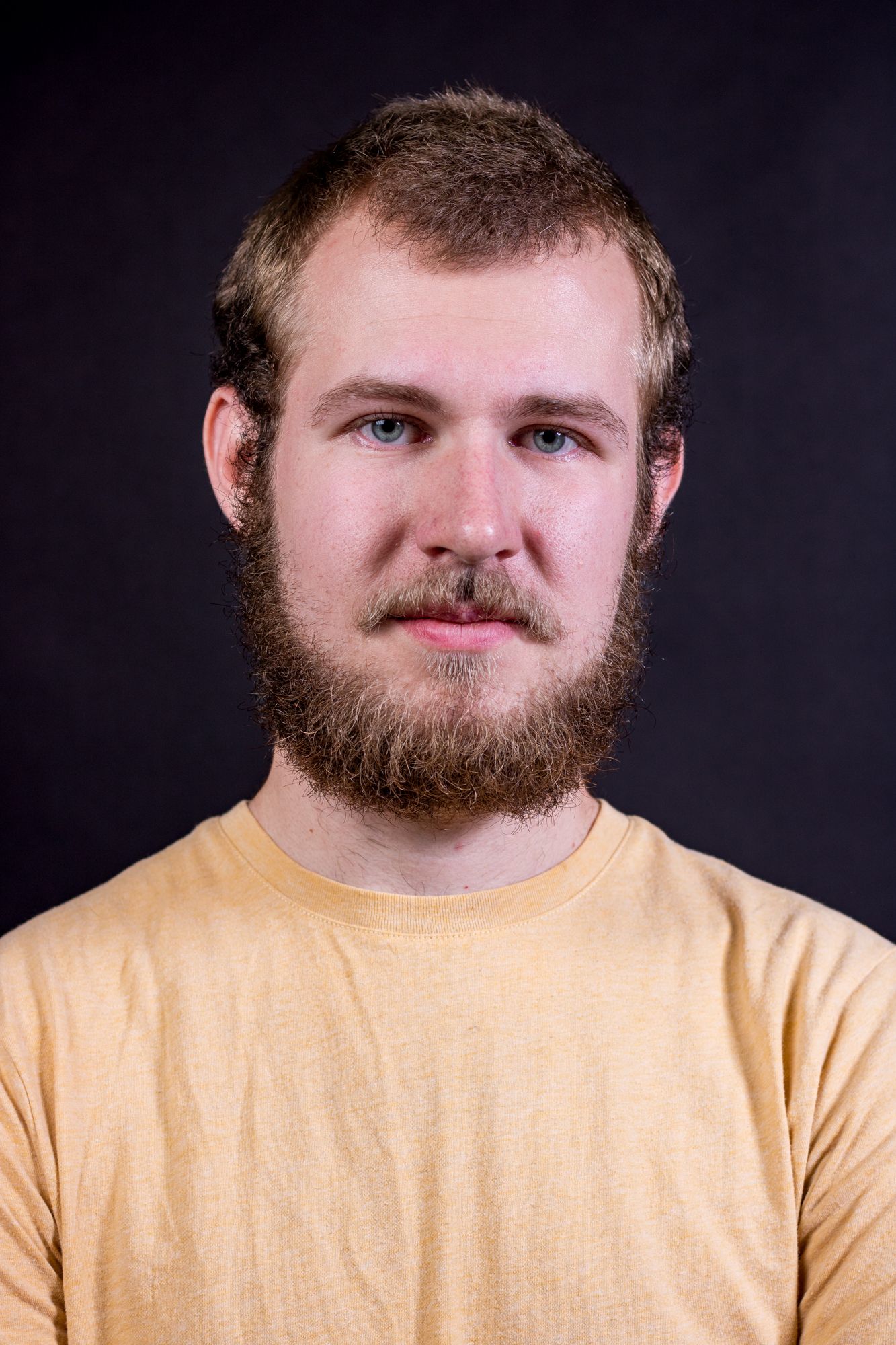 Portrait against dark background showing person in yellow t-shirt and full beard.