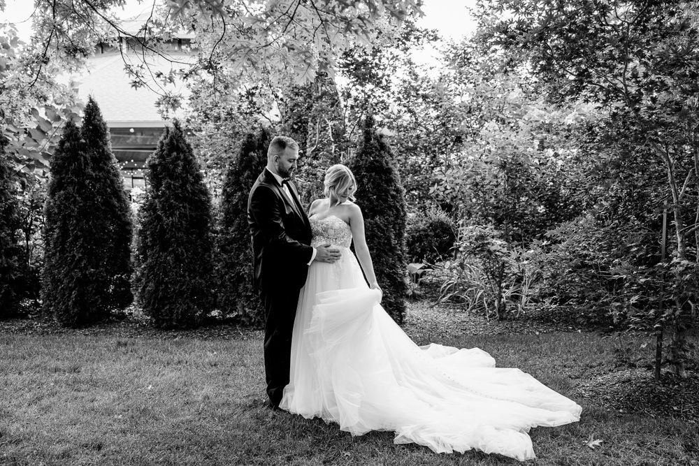 Black and white wedding portrait with a couple standing among evergreen trees.