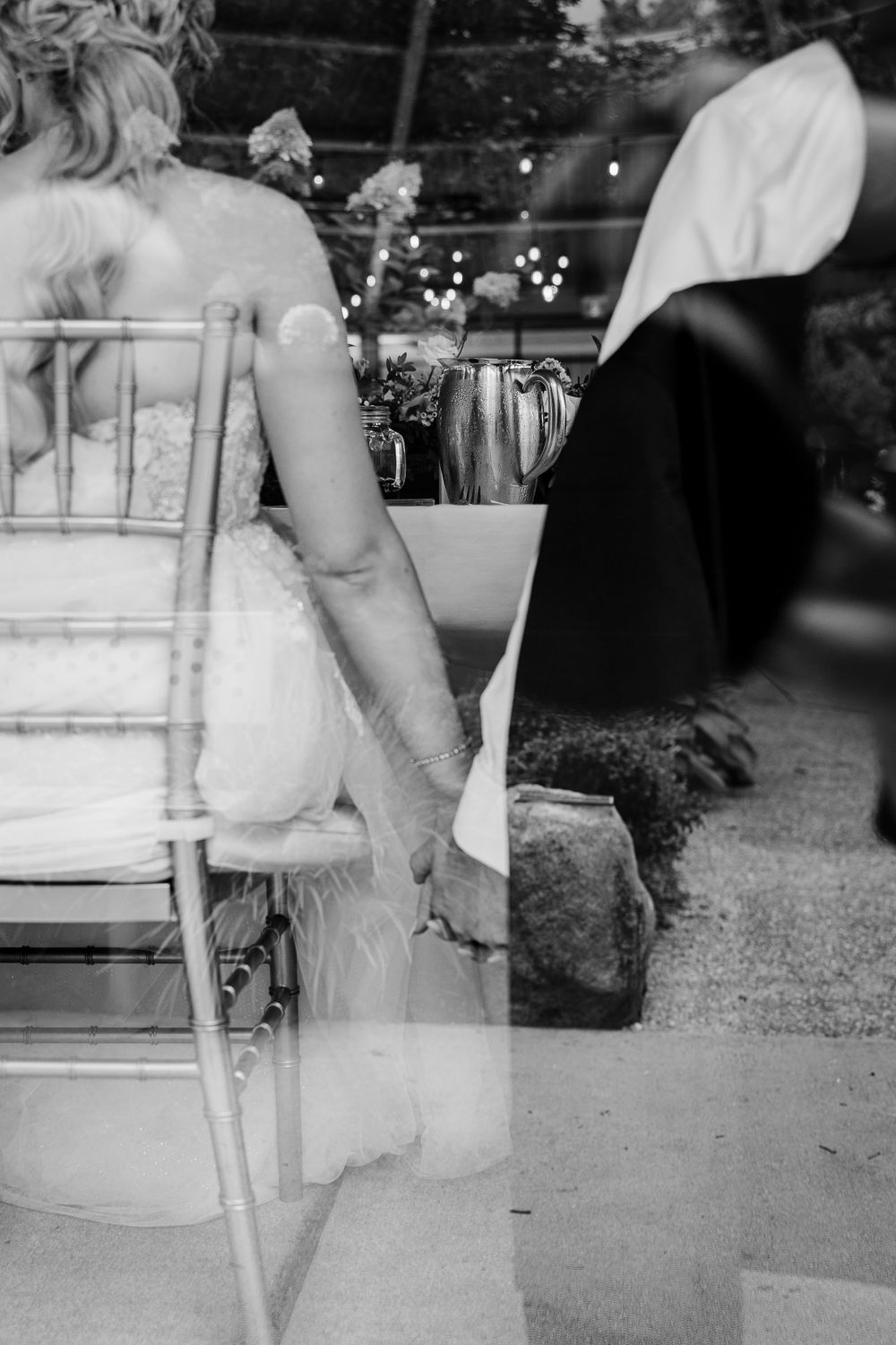 Black and white wedding detail shot of bride sitting in chair at outdoor venue.