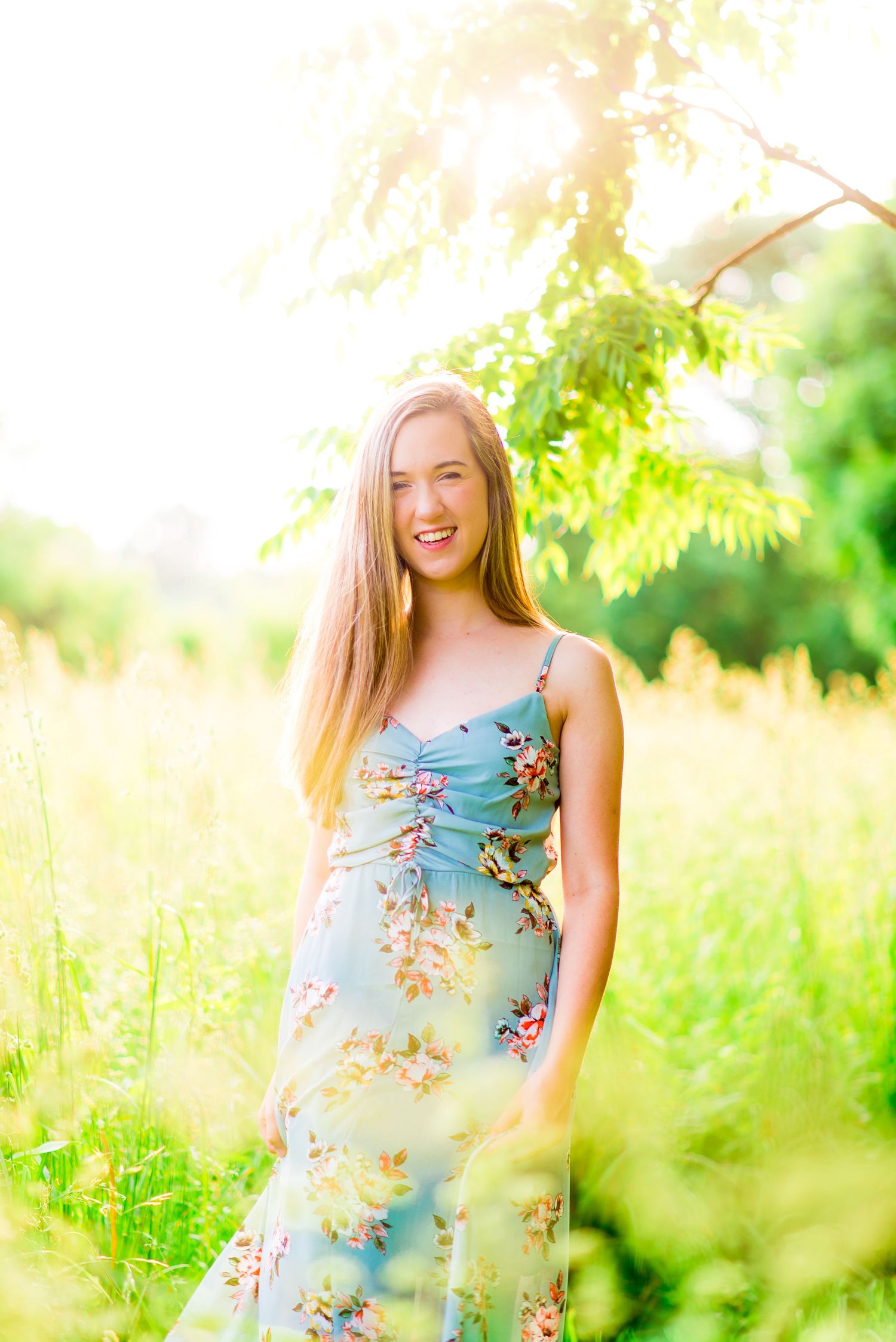 high school senior smiles in blue floral dress at sunset at Montrose Harbor in Chicago