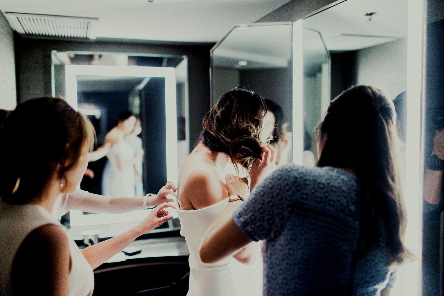 bride adjusting hair in front of mirror with friends helping