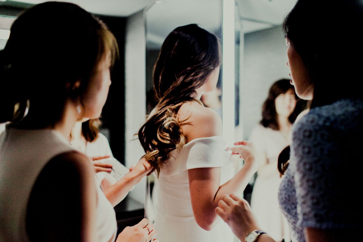 friends adjusting dress while bride getting ready