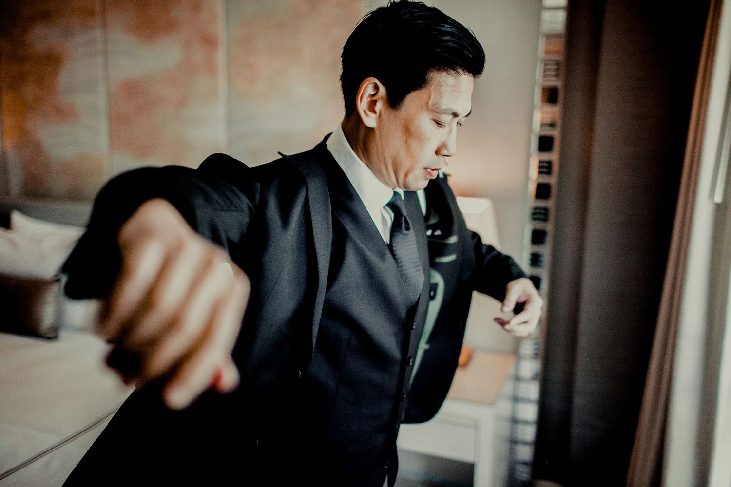 groom putting on blazer in front if window