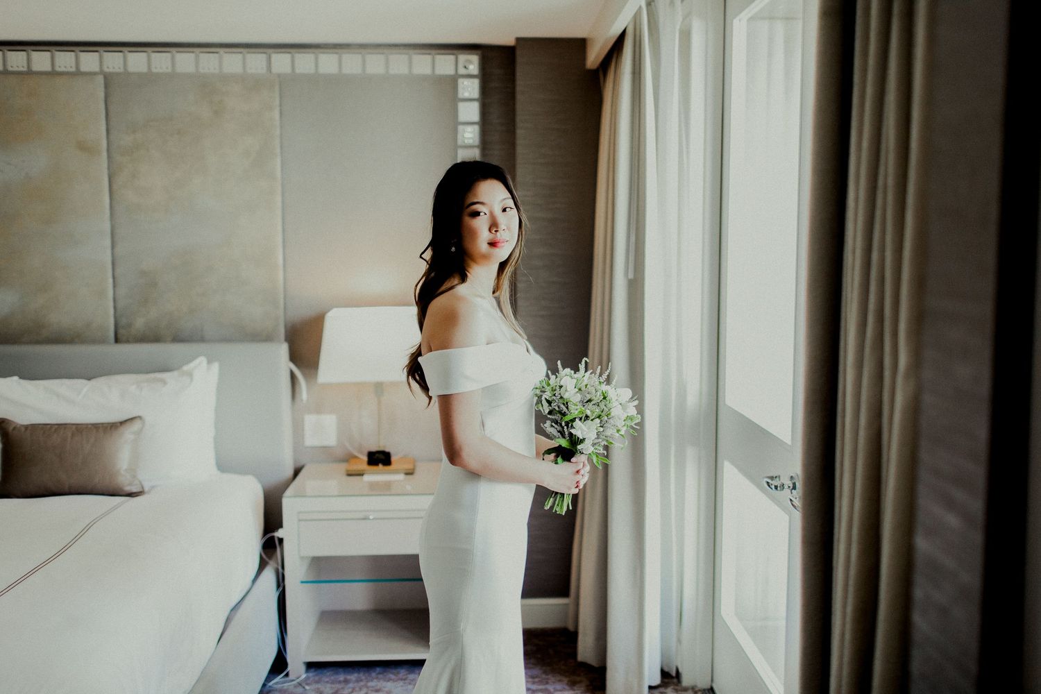 bride standing in front of window holding flowers