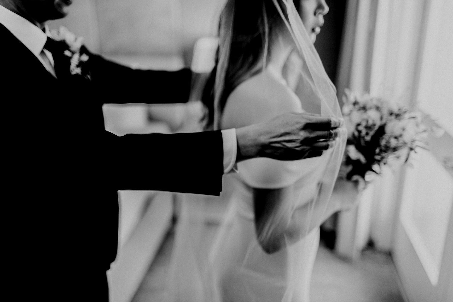 groom adjusting veil for bride in front of a mirror