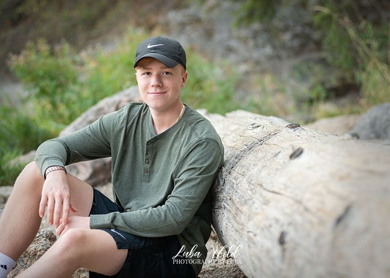 hs senior boy sitting by a log on a beach of Coeur d'Alene lake photographer luba wold