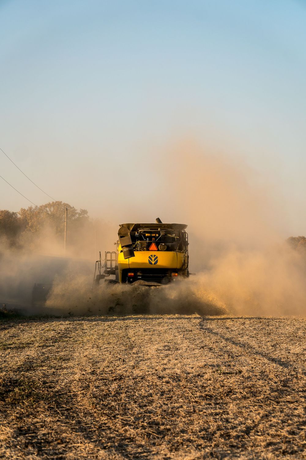 Yellow combine harvester kicking up dust while harvesting in dry field.