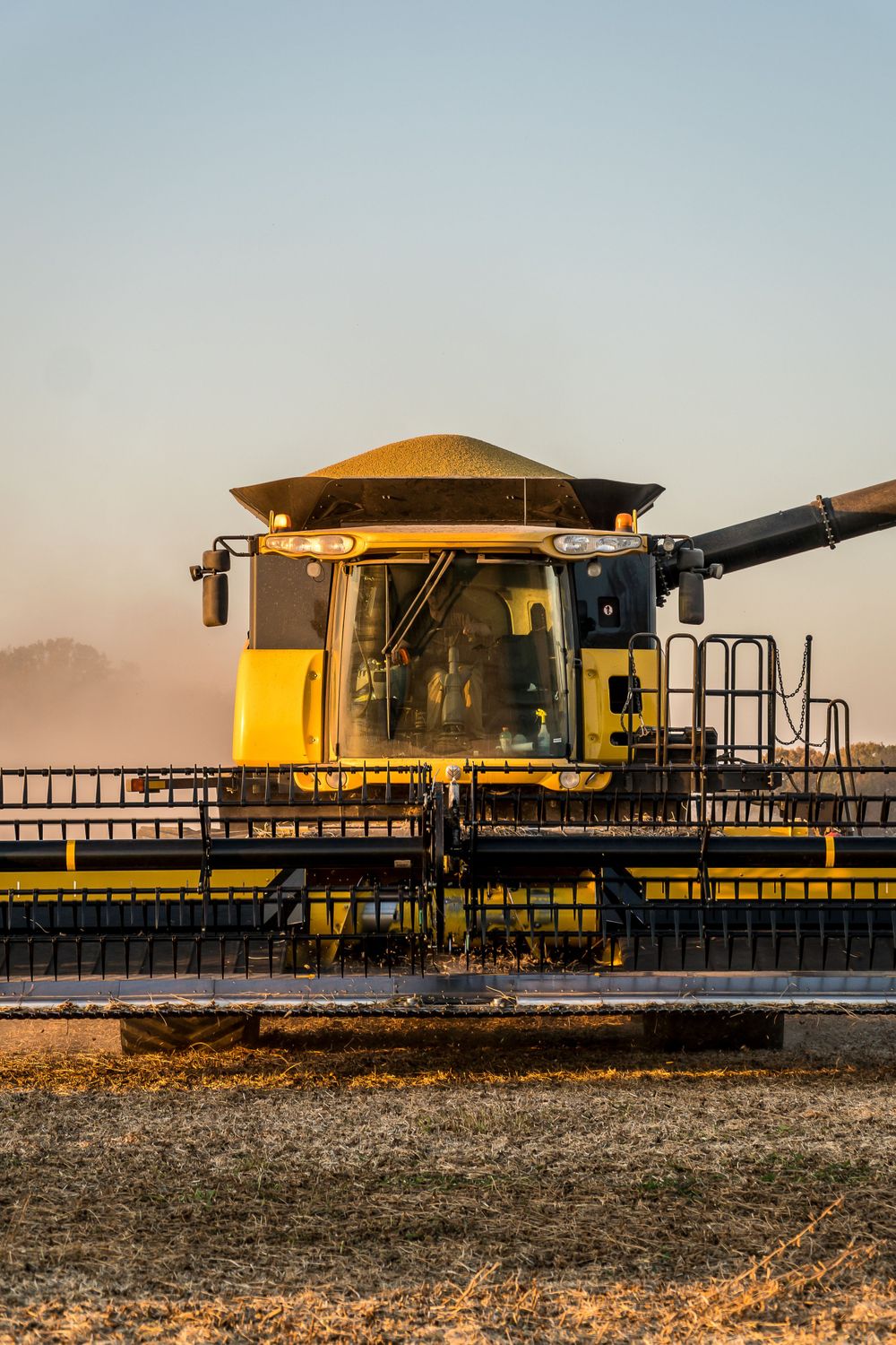 Close-up view of yellow combine harvester with large header attachment in field.