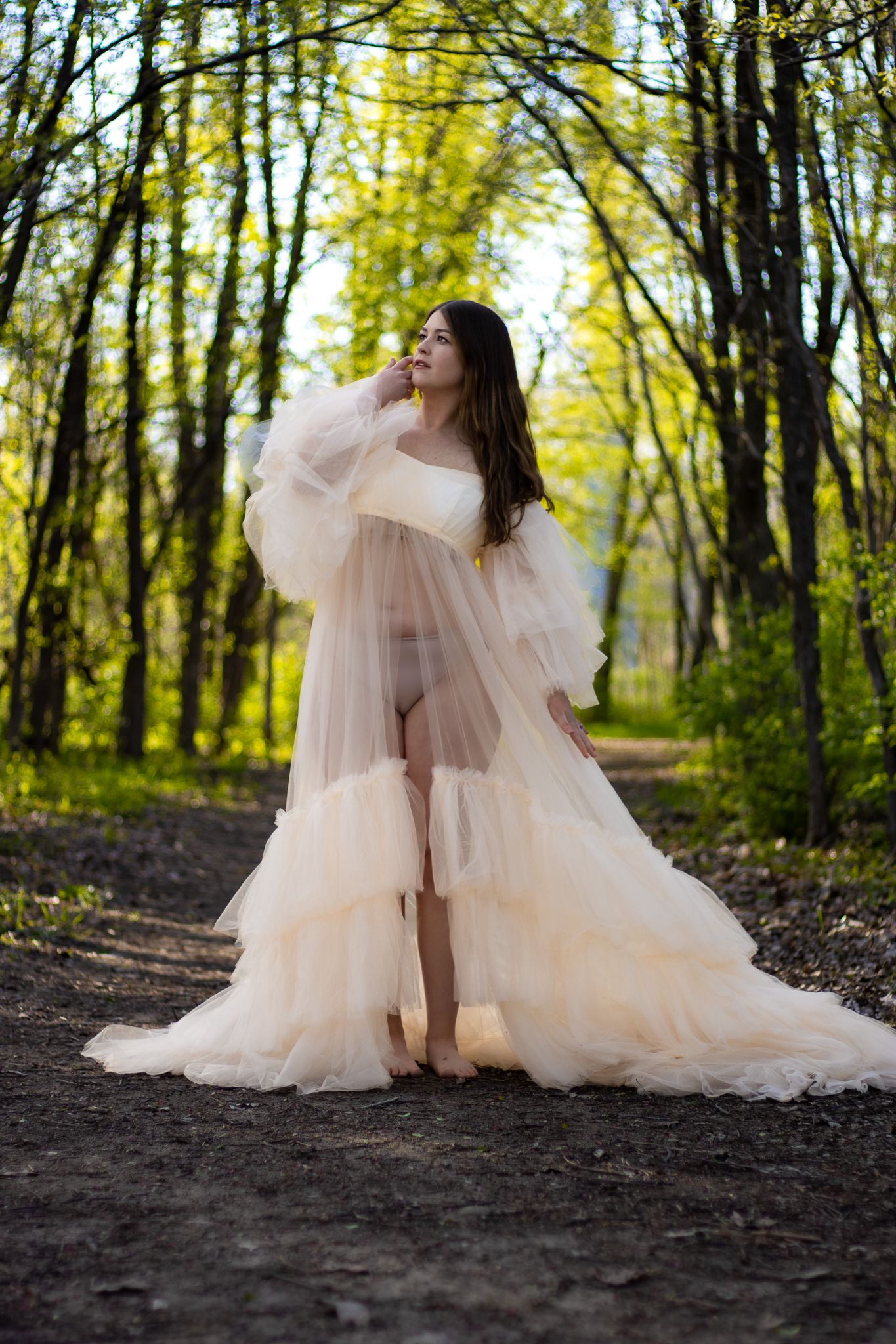 An ethereal cream tulle gown captured on a forest path with golden sunlight filtering through trees.