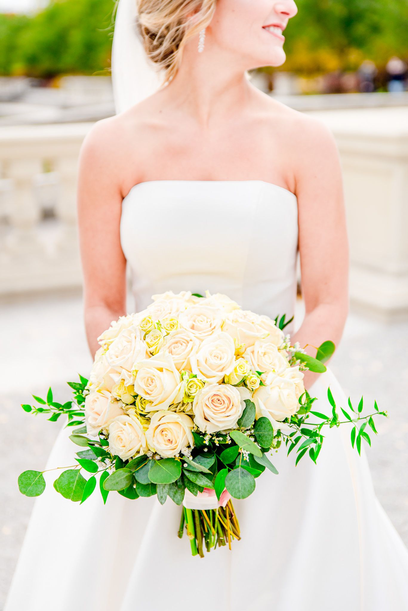 bride in strapless wedding dress holding white and green bouquet, looking to the side