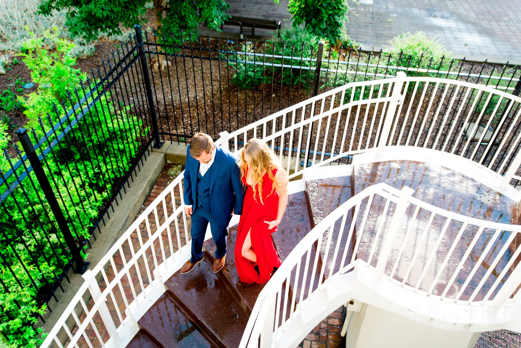 woman in red dress and man in navy suit walk down white staircase wet with rain at the Galt House Hotel