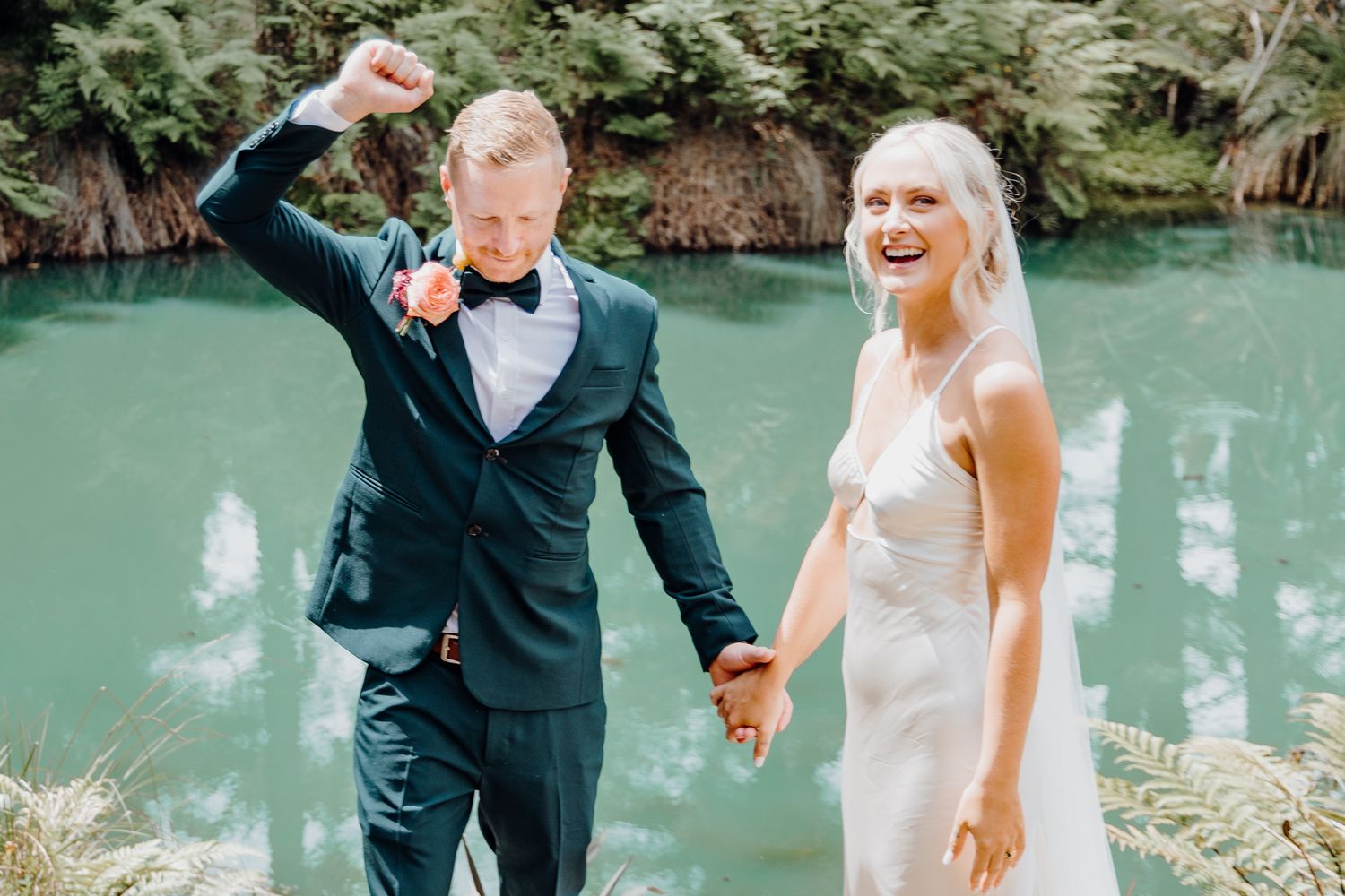 Joyful newlyweds celebrate after their ceremony by a stunning blue-green lagoon.