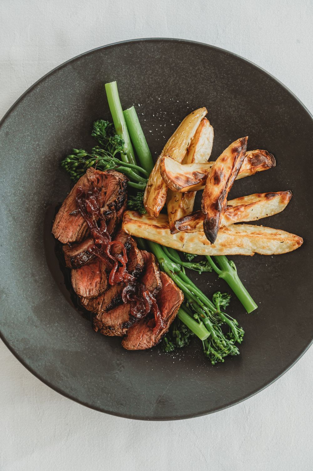 Seared steak with grilled shrimp, roasted potatoes and broccolini on a dark plate. SIX84 Photography, Food Photography, Sydney