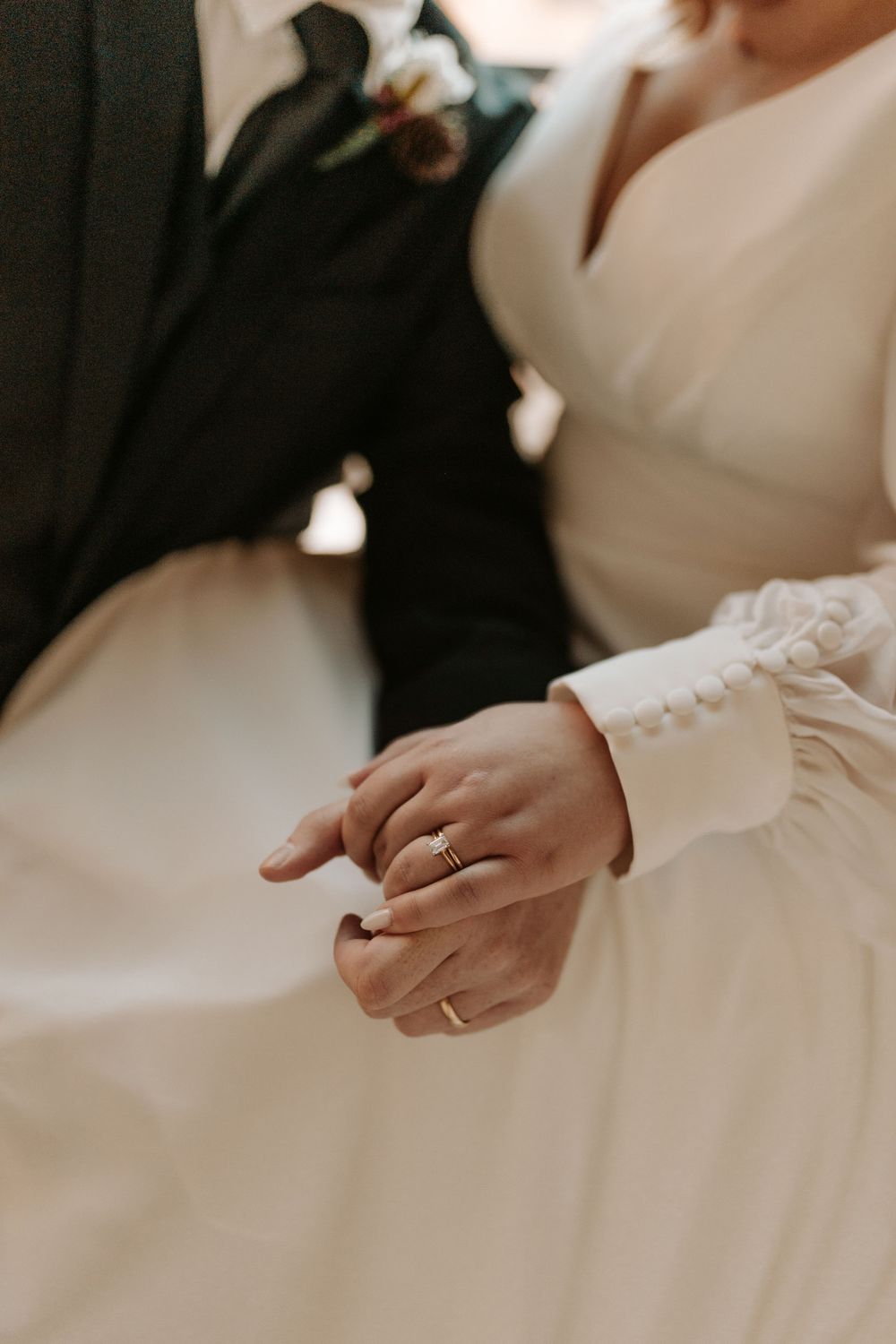 Close-up of an elegant wedding ring on the bride's hand against the backdrop of a white wedding dress.
