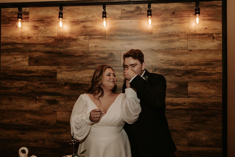 Romantic wedding couple pose against rustic wooden wall with warm lighting.