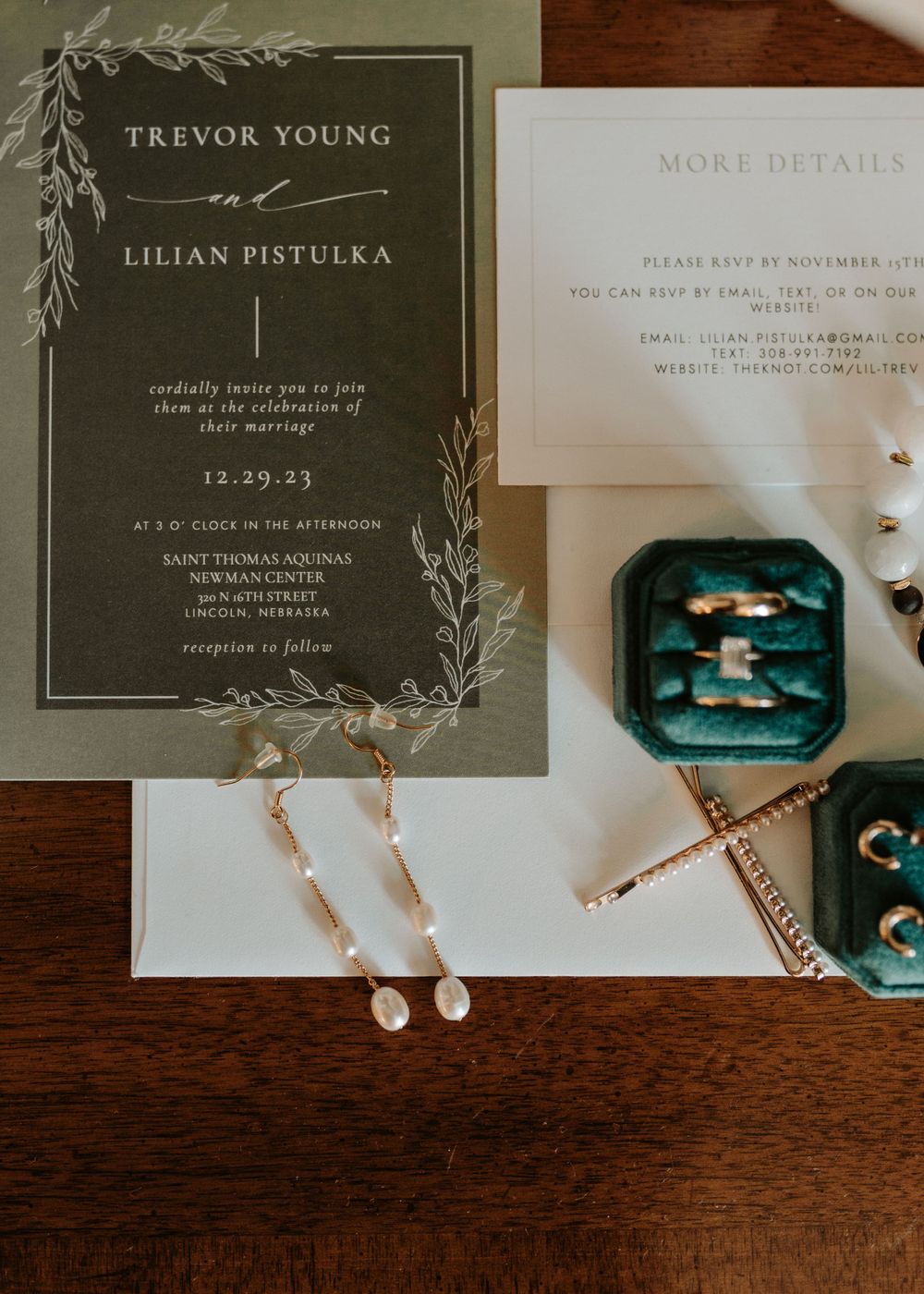 Elegant wedding invitation with botanical details and jewelry displayed on dark wood surface.