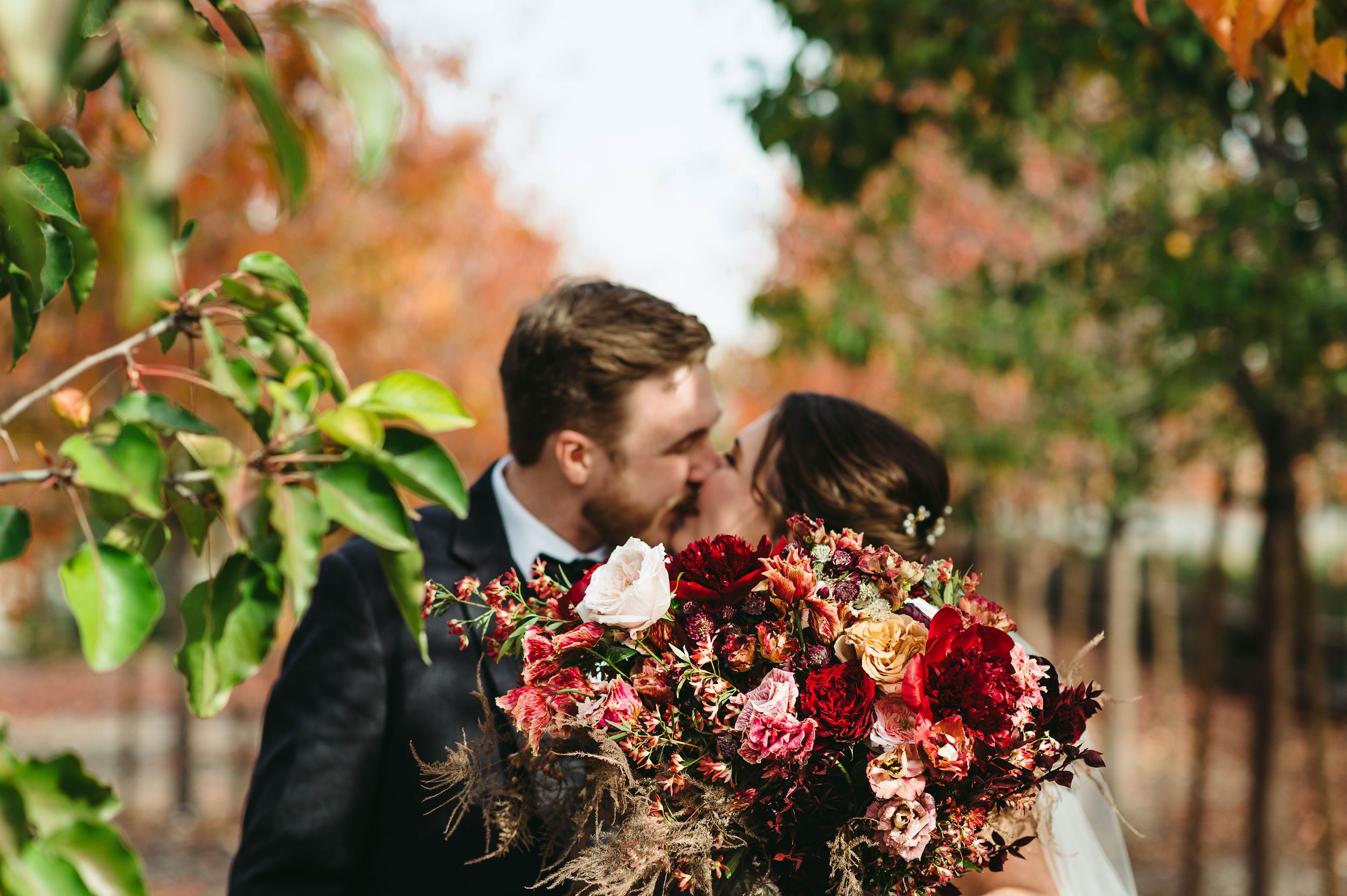 Bride and groom kissing behind a big red bouquet of flowers.