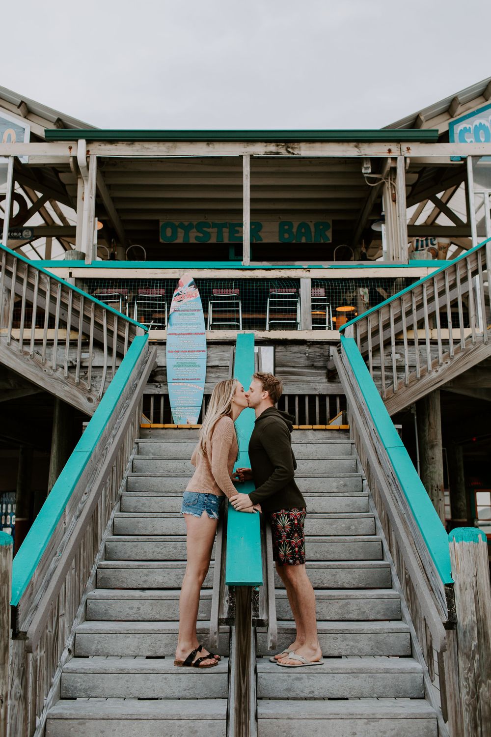 man and woman standing on opposite sides of a staircase sharing a kiss on the Okaloosa Island Boardwalk