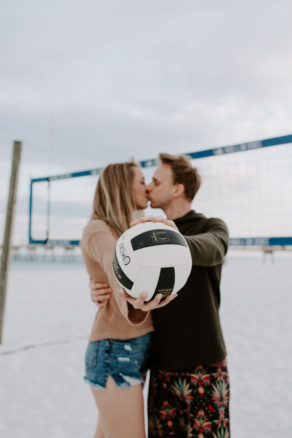 couple kissing as they are hooding volleyball out in front of them