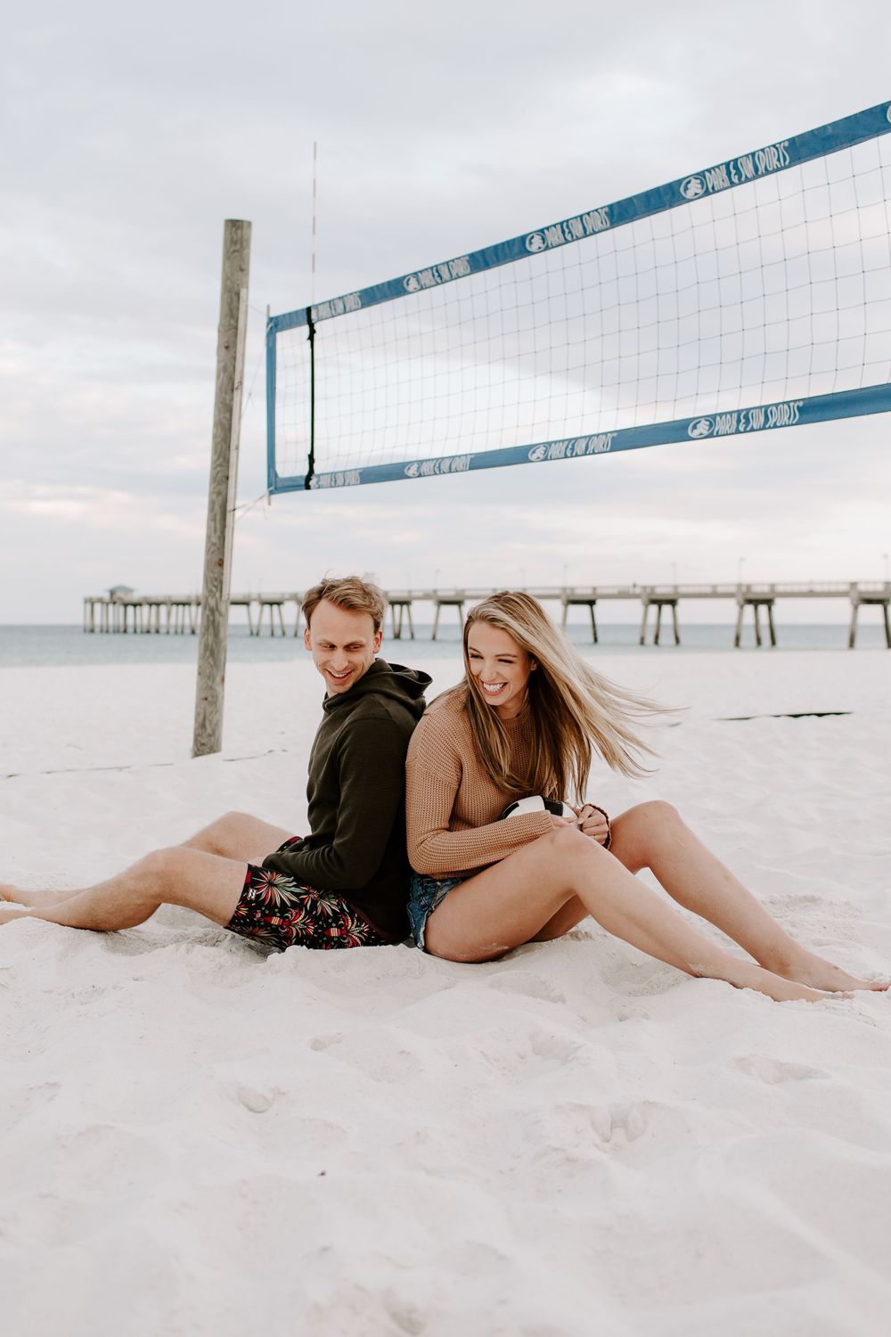 couple sitting back to back in the sand of a volleyball court during their Destin couples photo session