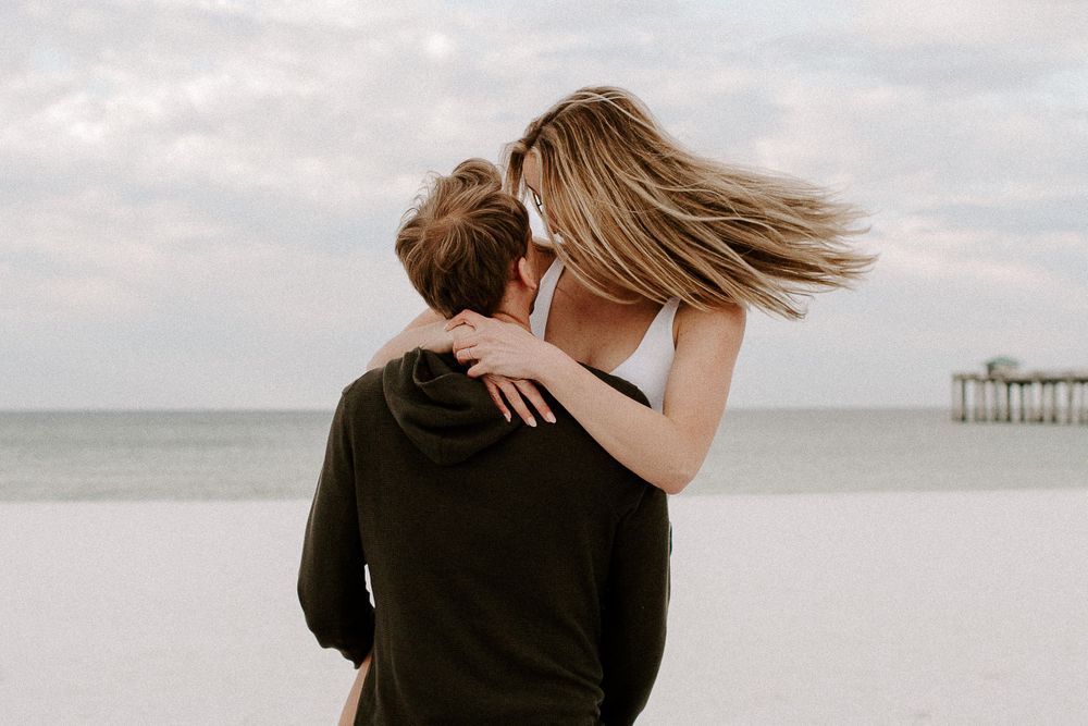 man picking up his fiancé and spinning her in a circle as her hair blows in the wind
